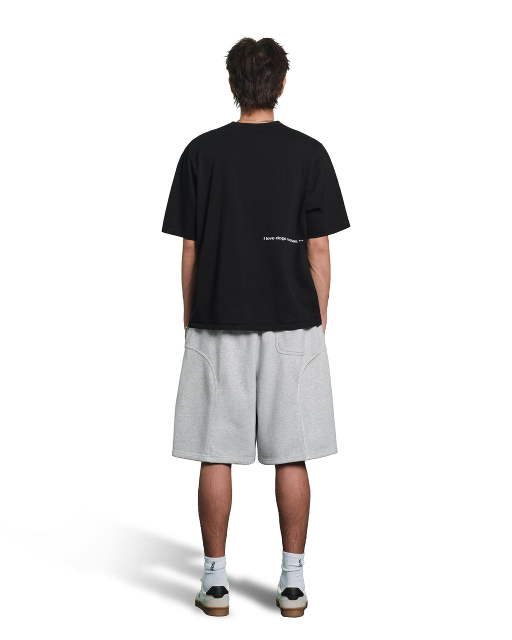 A model shown from the back wearing an oversized black t-shirt with small white text on the back, light gray heathered shorts, white socks, and sneakers, against a plain white background.