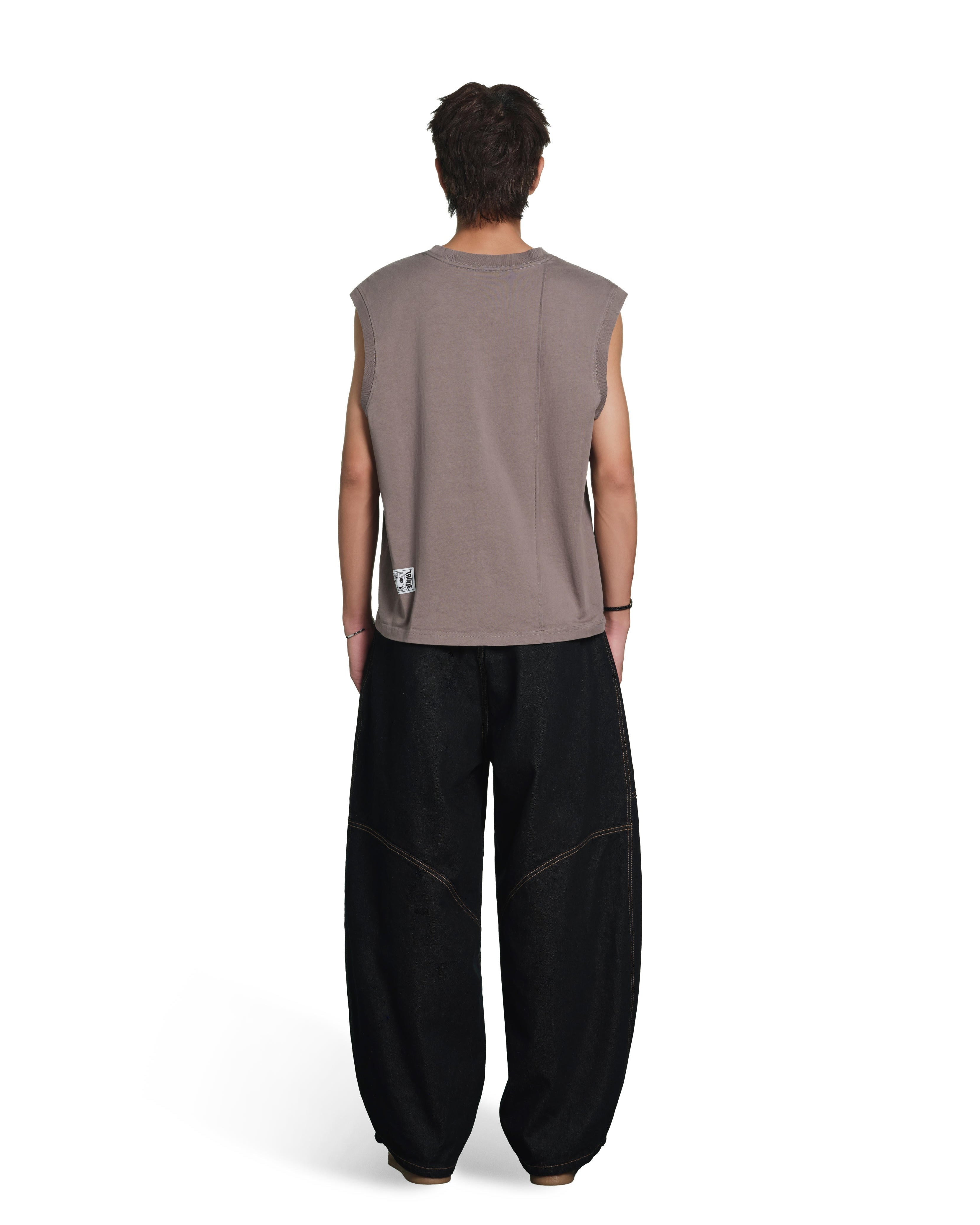 A model shown from the back wearing a sleeveless taupe-brown t-shirt and loose black pants, photographed against a solid white background.