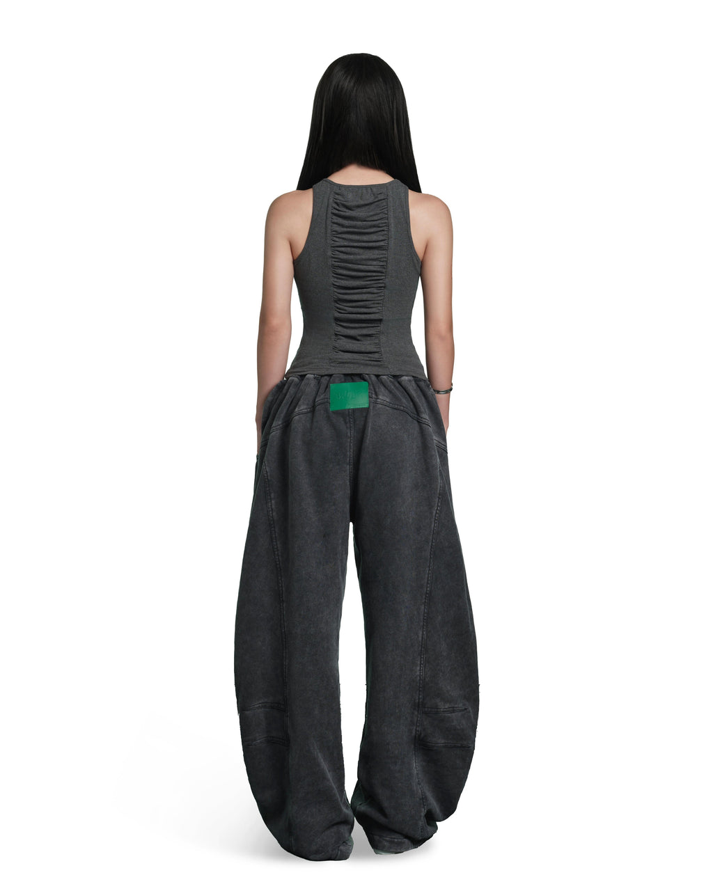 A model shown from the back wearing a dark gray sleeveless top with a ruched back and matching wide-leg pants, featuring a bright green accent patch at the waist, on a solid white background.
