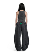 A model shown from the back wearing a dark gray sleeveless top with a ruched back and matching wide-leg pants, featuring a bright green accent patch at the waist, on a solid white background.