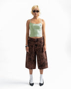 A model stands against a white studio background wearing a light green camisole, brown patterned cropped pants, white socks, and black shoes.