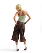 A woman with short blonde hair is shown from behind wearing a light green cutout camisole, brown patterned cropped pants, white socks, and black high heels against a plain white background.