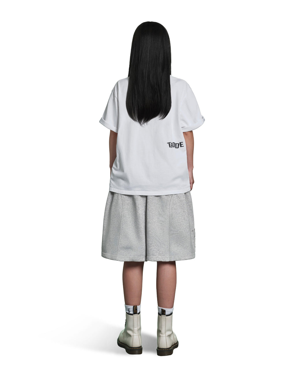 A child model shown from the back wearing a white oversized T-shirt with a small black 'TIDE' logo on the left side, light gray shorts, and off-white ankle boots, against a plain white background.