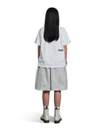 A child model shown from the back wearing a white oversized T-shirt with a small black 'TIDE' logo on the left side, light gray shorts, and off-white ankle boots, against a plain white background.
