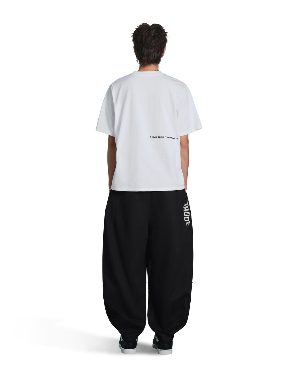 A model shown from the back wearing a white t-shirt with small black text on the back and black baggy sweatpants with a white vertical logo on the left leg, set against a plain white background.